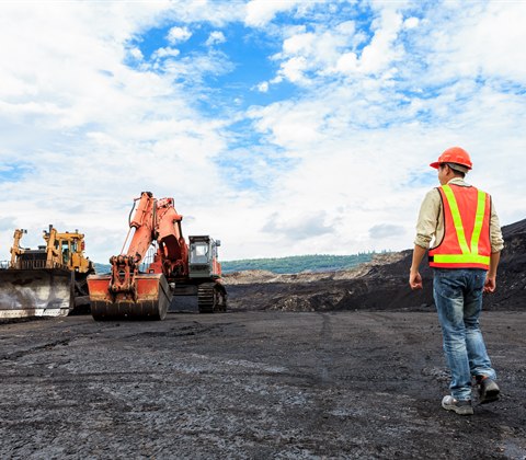 Supervisor walking towards excavators working an open-cut mine bench