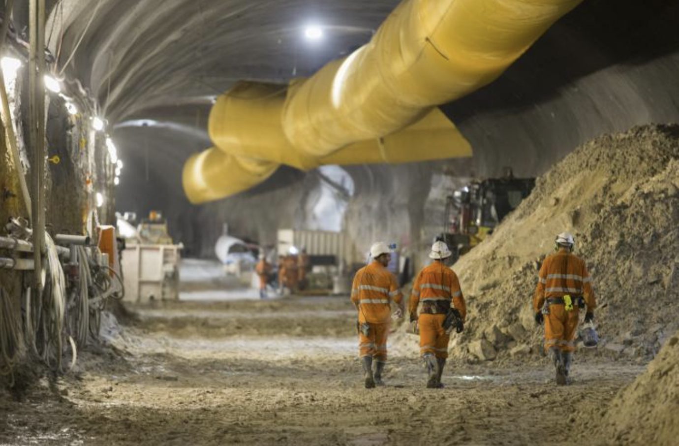 Workers walking through a tunnel under construction beside ventilation ducting