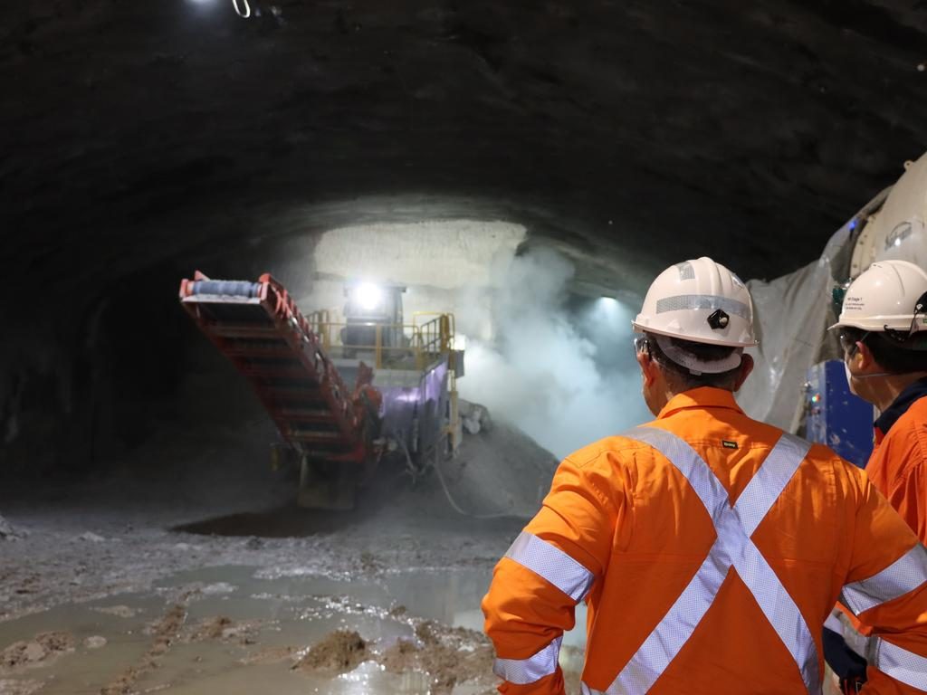Worker in orange high-visibility clothing watching a conveyor operating in an underground tunnel