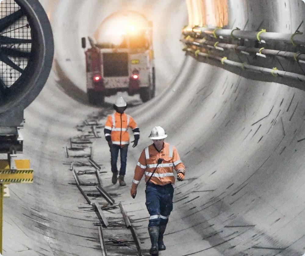 Two workers walking through a tunnel under construction with an emergency vehicle behind them