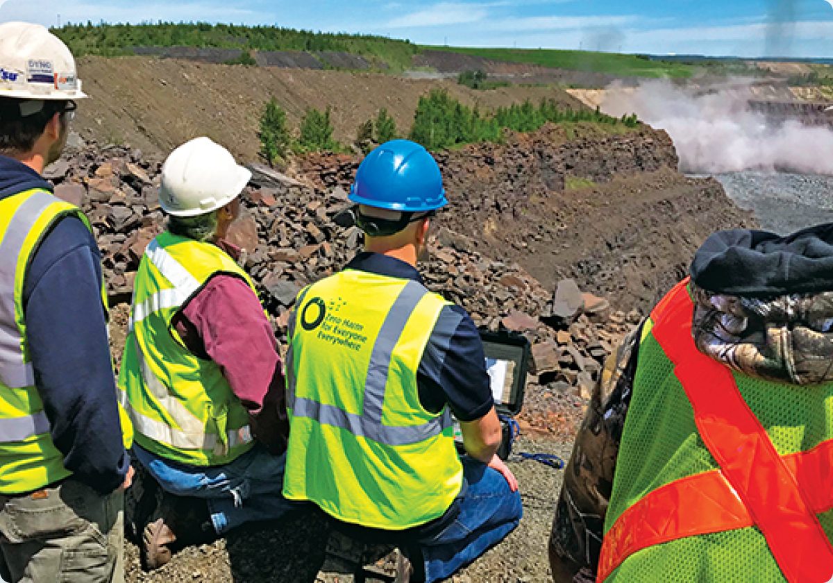Site team in high-visibility vests reviewing plans on a tablet above an open mining pit