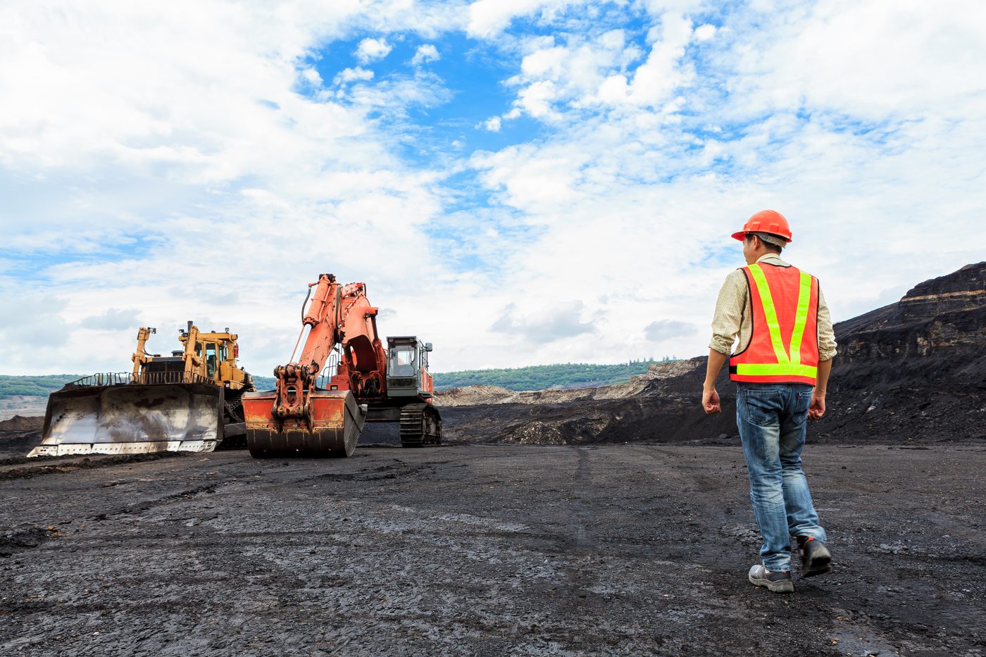 Excavators loading a haul truck on a mine bench as a worker in high-visibility clothing walks past